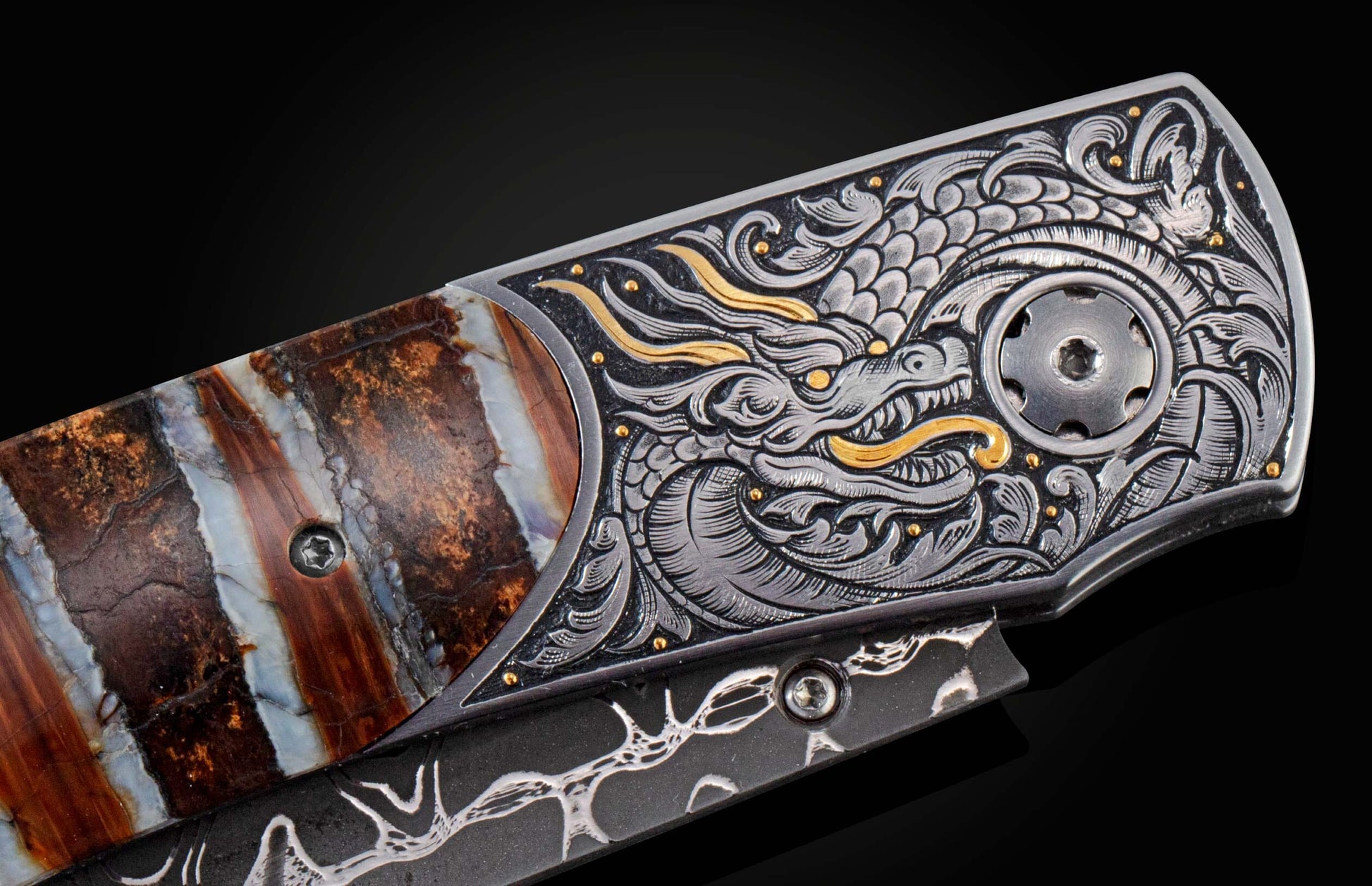 Ornate folding knife with a silver and gold dragon engraving, featuring a striped natural stone handle and a dark patterned blade, side view.