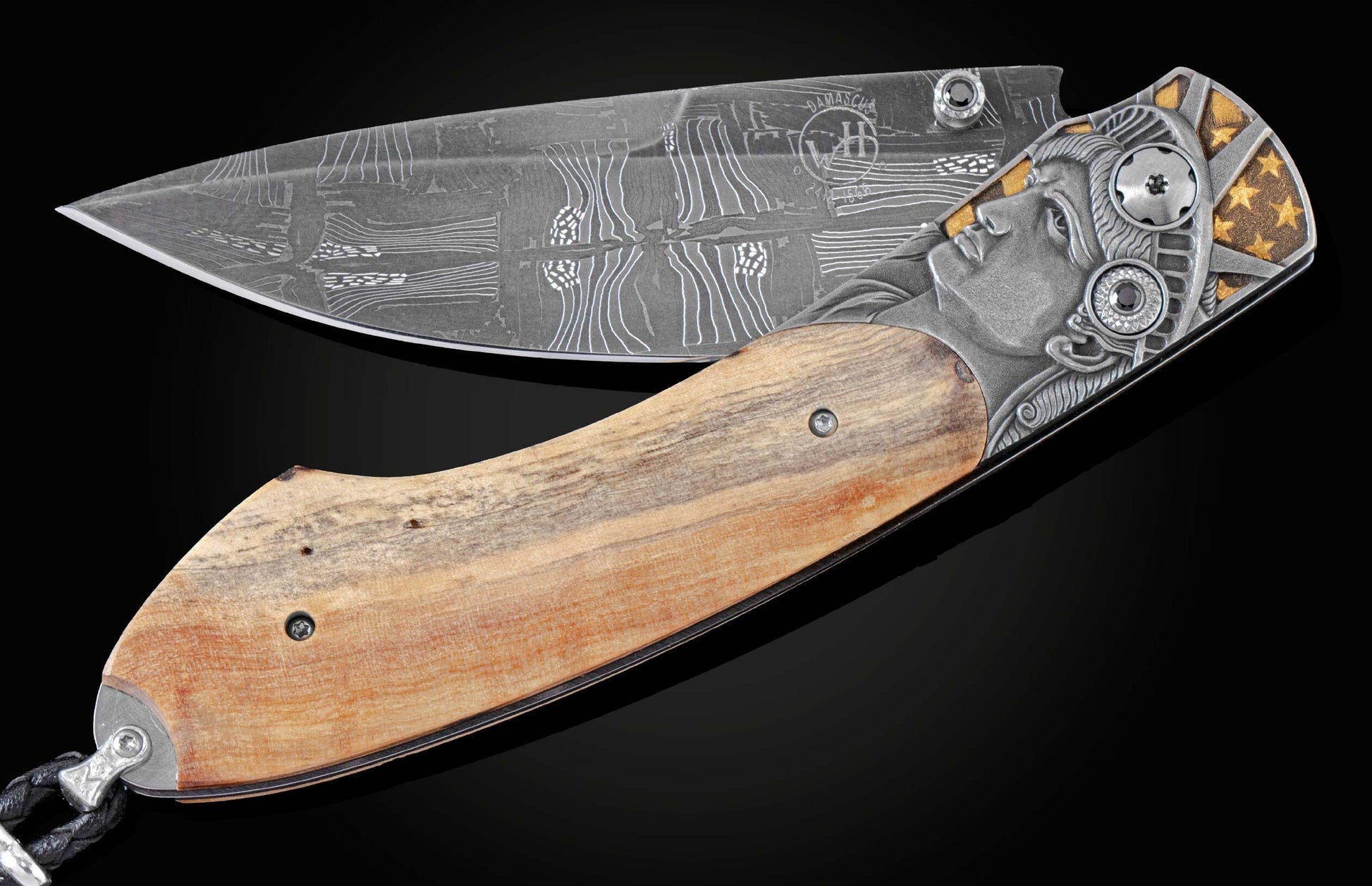 Handcrafted knife from William Henry features hand-engraved depictions of George Washington and the Statue of Liberty inlaid with a wood scale from trees planted by George Washington and set with spinel gemstones.. The blade is hand-forged damascus steel.