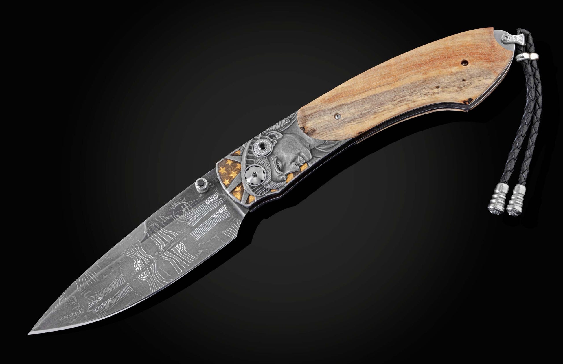 Handcrafted knife from William Henry features hand-engraved depictions of George Washington and the Statue of Liberty inlaid with a wood scale from trees planted by George Washington and set with spinel gemstones.. The blade is hand-forged damascus steel.