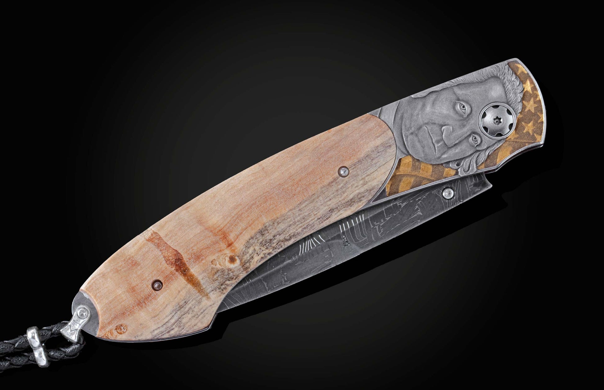 Handcrafted knife from William Henry features hand-engraved depictions of George Washington and the Statue of Liberty inlaid with a wood scale from trees planted by George Washington and set with spinel gemstones.. The blade is hand-forged damascus steel.