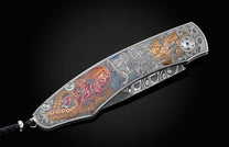 Handcrafted pocket knife from William Henry features beautiful color laser engraving of pirate scenes by Bottega Incisioni in Italy and set with spinel gemstones. The blade is damascus  steel.