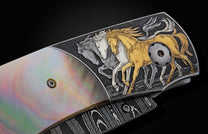 Handcrafted knife from William Henry featuring hand-engraved horses with 24K gold and silver inlays and scales of black lip pearl and stud are set with spinel gemstones. The Damascus steel blade is hand-forged with Gibeon Meteorite.