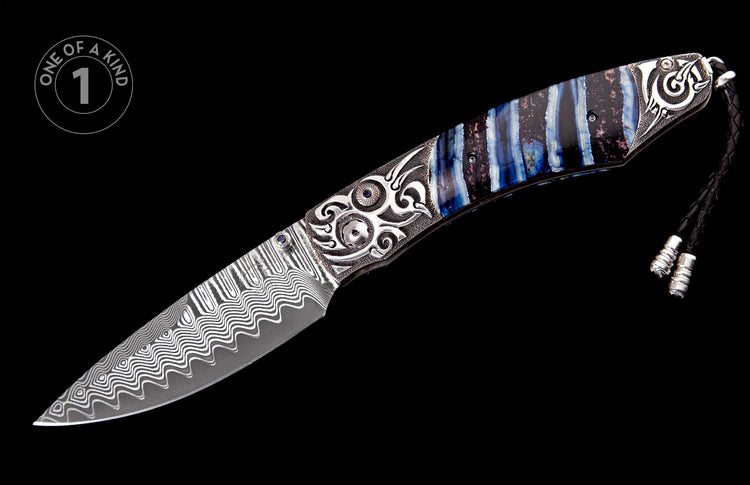 Ornate folding knife featuring a wavy Damascus steel blade, blue striped handle, intricate silver bolsters with a blue gem, and a black leather lanyard.