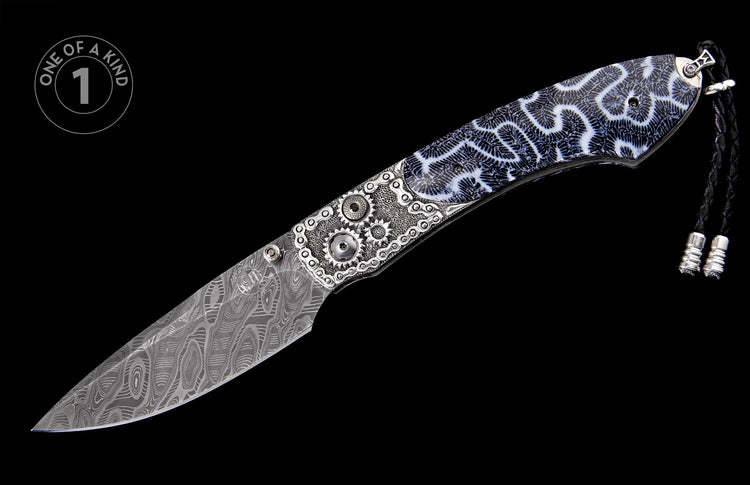 Knife with a wavy Damascus steel blade, intricate silver-toned gear and chain-link metalwork, black and white coral-patterned grip, and braided black lanyard.