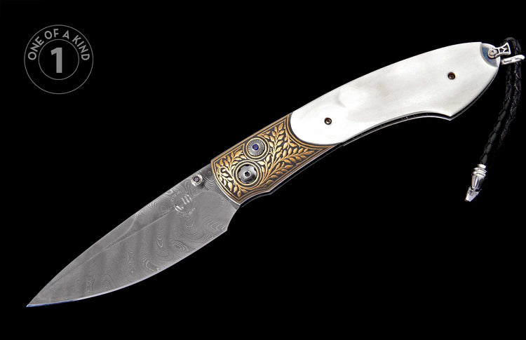 Ornate folding knife with white handle, Damascus blade, gold leaf engraving, blue gemstone accents, and a braided leather lanyard.