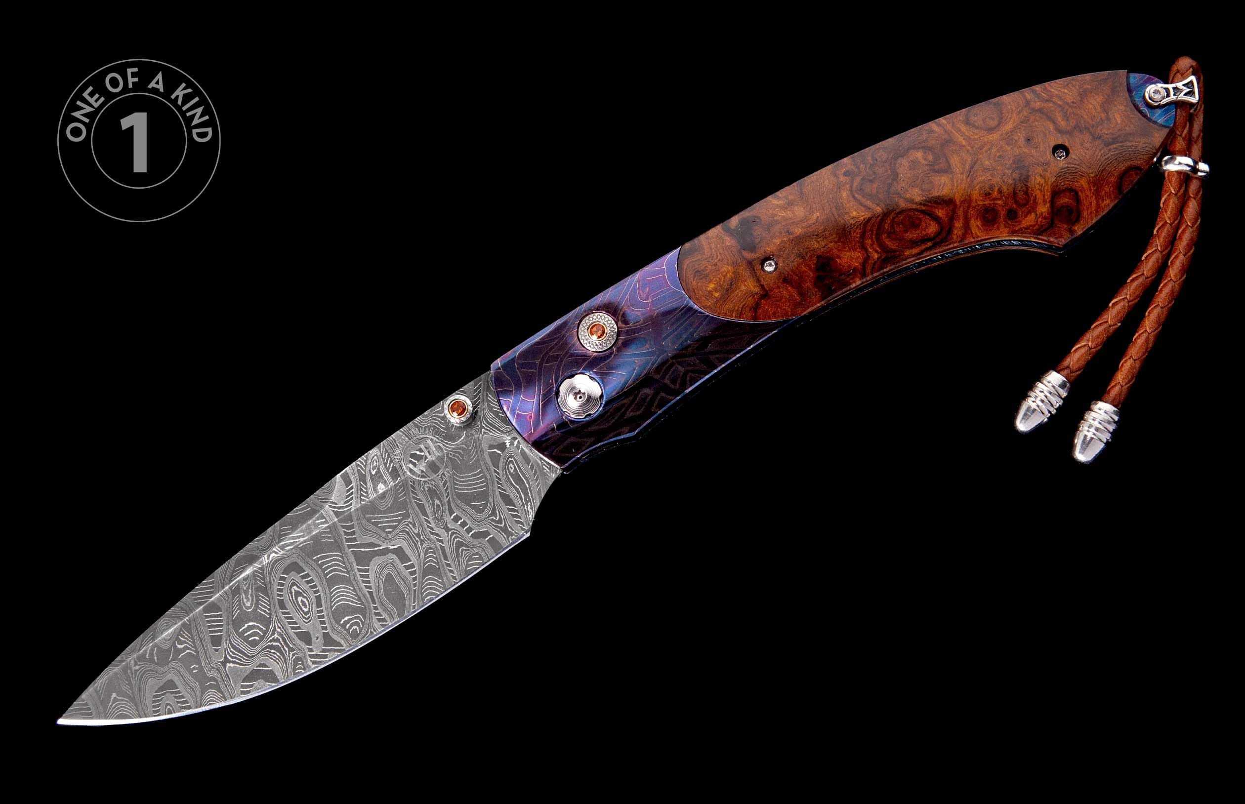 Artisan folding knife with a wavy Damascus steel blade, burl wood and engraved purple metallic handle, and a brown leather lanyard.