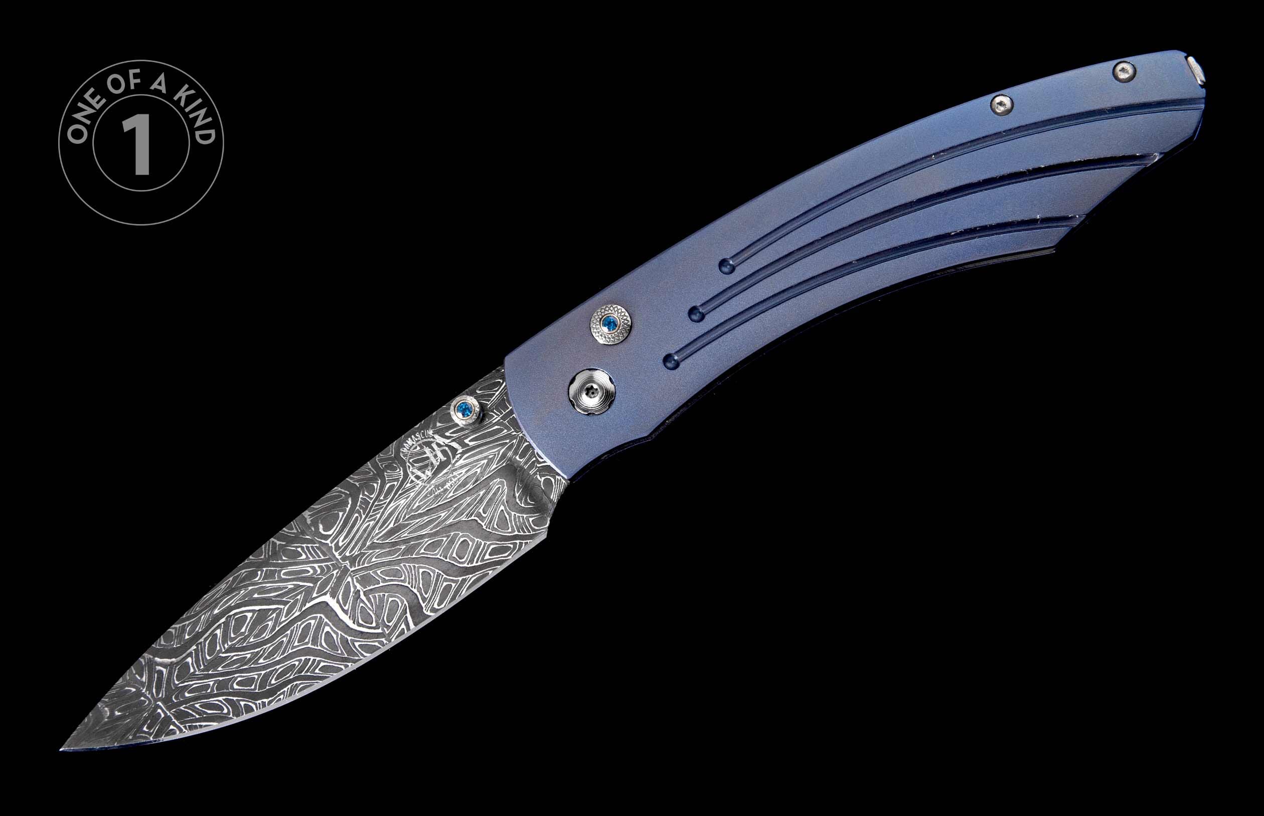 Blue handled knife with an intricately patterned Damascus steel blade and blue jewel accents, viewed diagonally.
