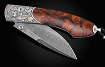 Handcrafted pocket knife from William Henry features hand and laser-engraved koi fish with copper and brass,, inlaid with desert ironwood, smoky quartz gemstones. and a hand forged Damascus steel blade.
