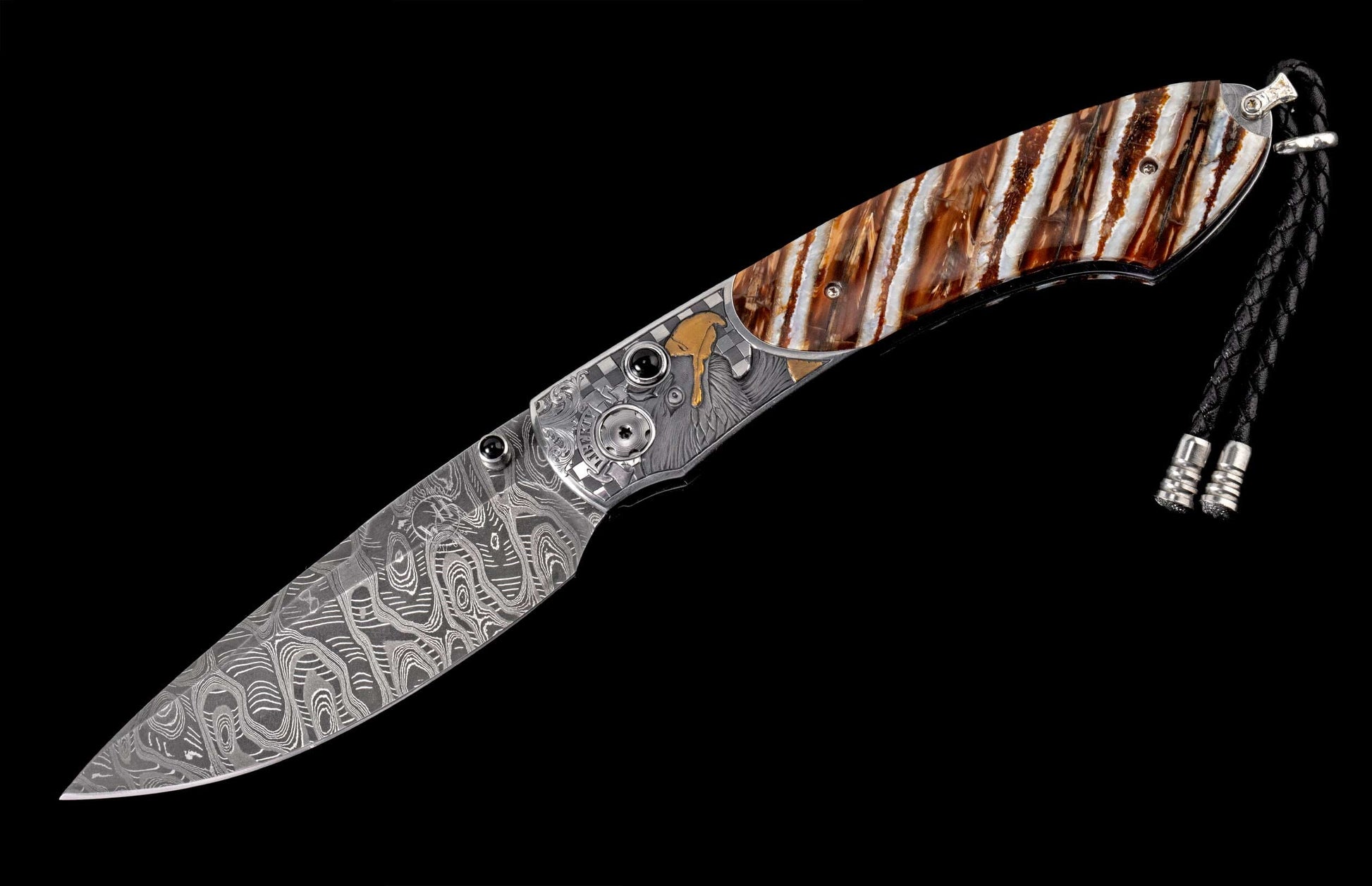 Ornate folding knife with a patterned Damascus steel blade, brown and white striped handle, engraved silver frame with an eagle head and gold accents, and a black braided lanyard.