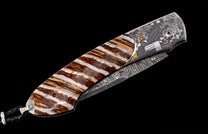 Folding knife with striped brown and white handle, intricately engraved metal frame featuring an eagle and 'JUSTICE' text, Damascus blade, and braided leather lanyard.