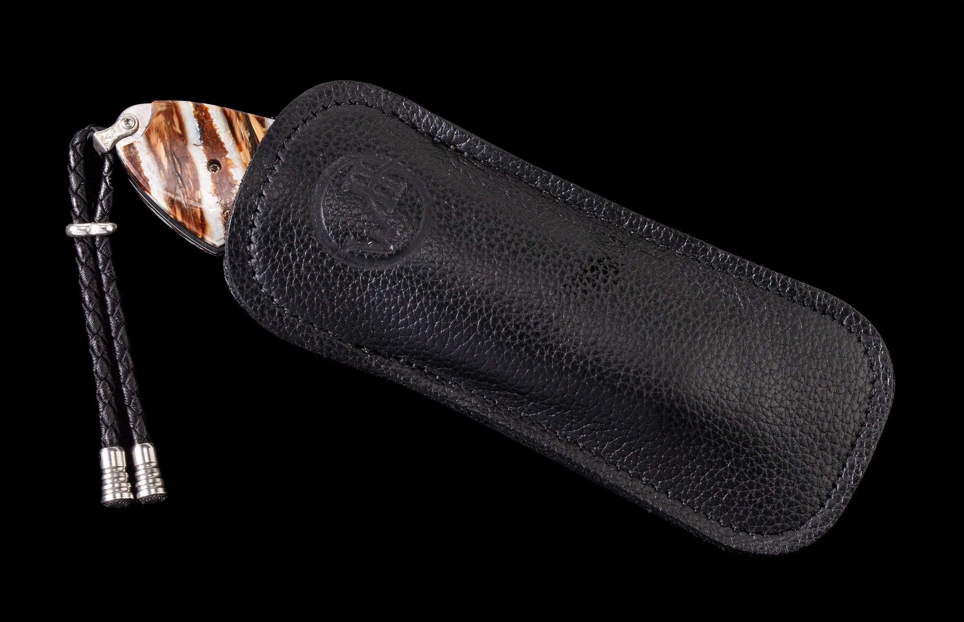 Striped brown and white knife by Liberty & Justice partially sheathed in a textured black leather pouch with an embossed logo and braided lanyard.