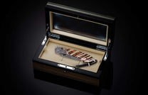 Folding knife with a brown and white striped handle, eagle engraving, Damascus blade, and braided lanyard, displayed in an open dark wood grain box.