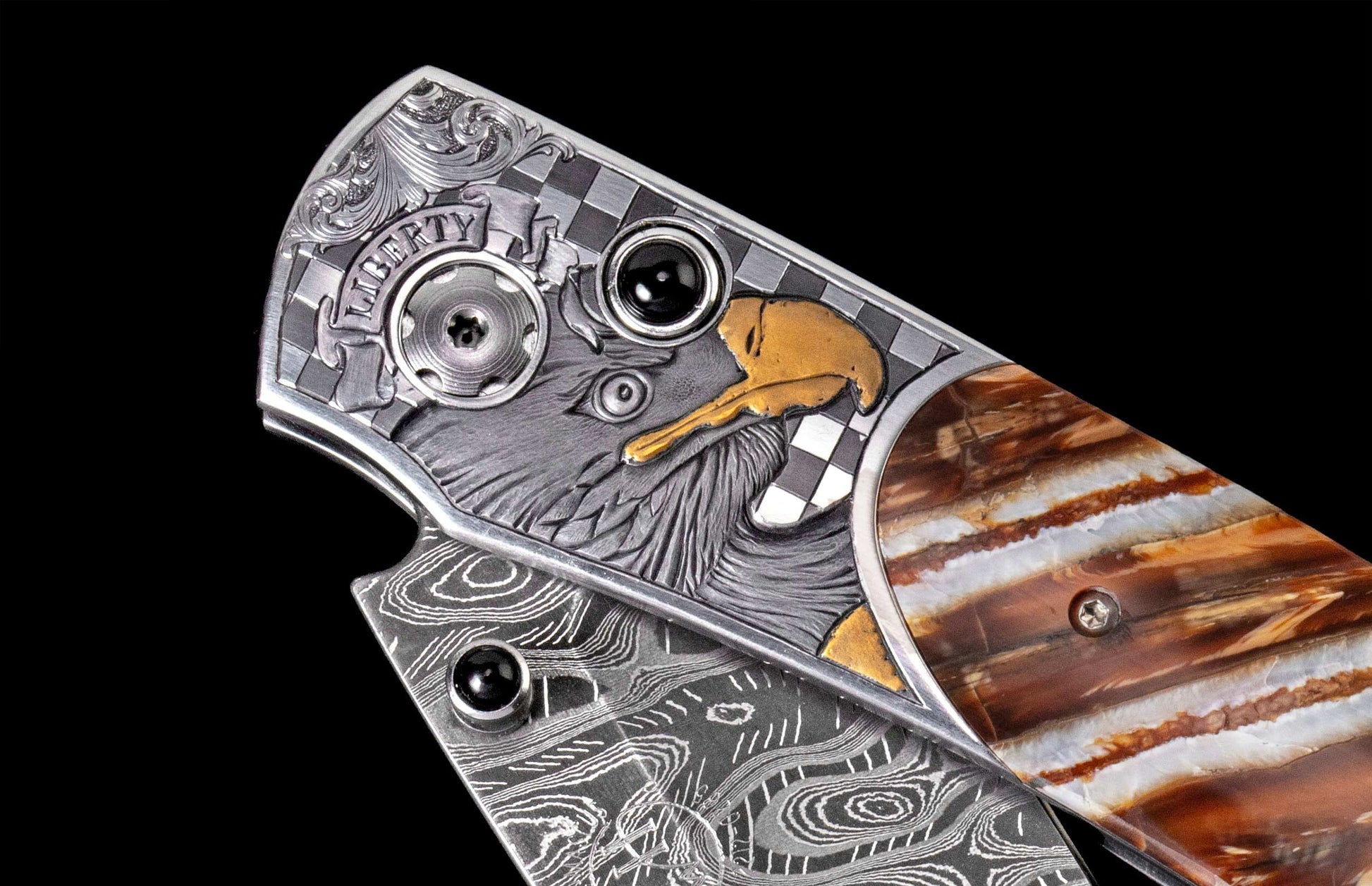 Engraved knife featuring a silver-tone eagle head, 'LIBERTY' banner, gold accents, checkerboard, and a brown striped handle with a Damascus blade.