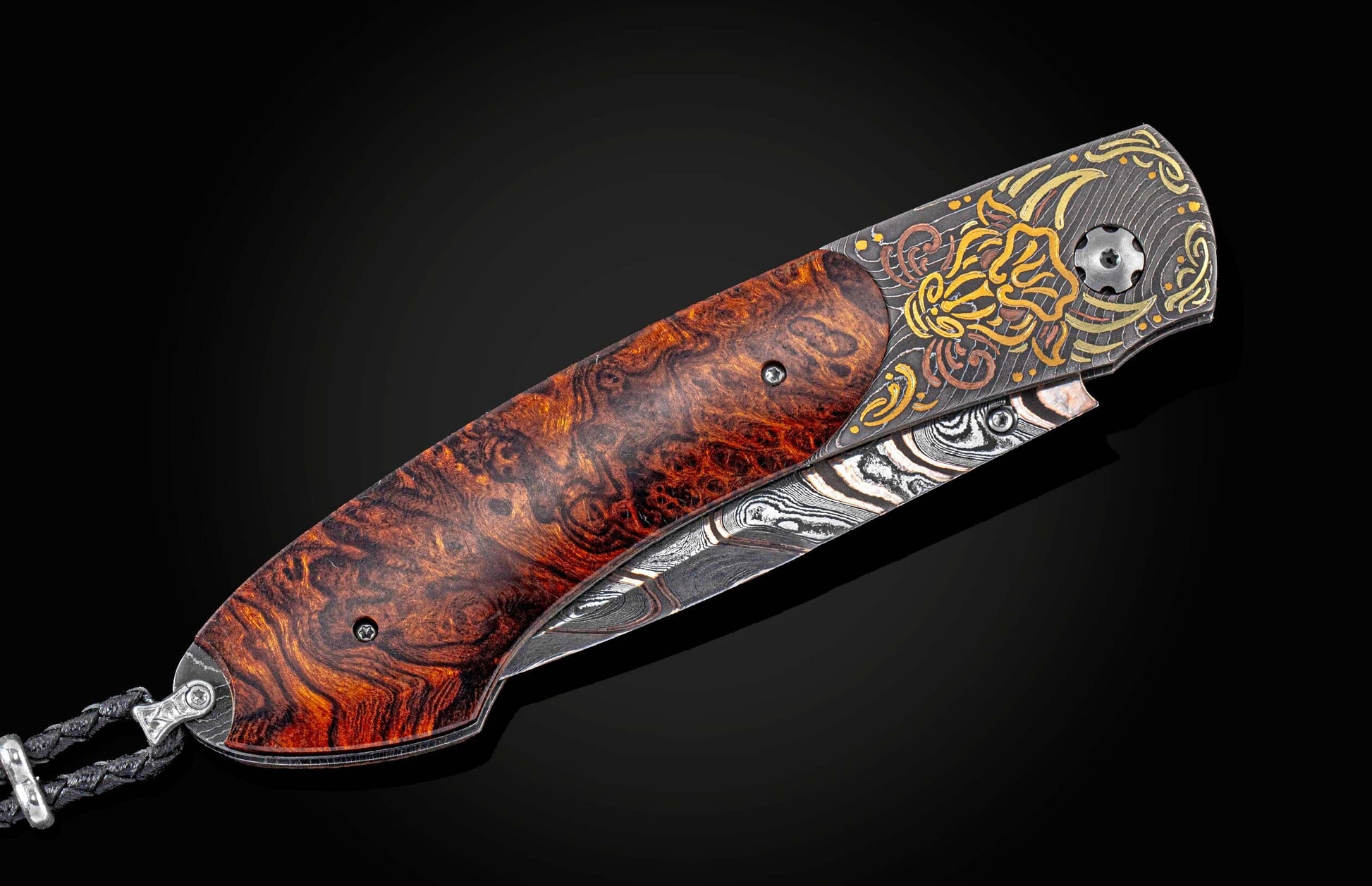 Angled folding knife with a dark burl wood handle, patterned Damascus blade, and ornate etched metal bolster featuring gold and bronze accents.
