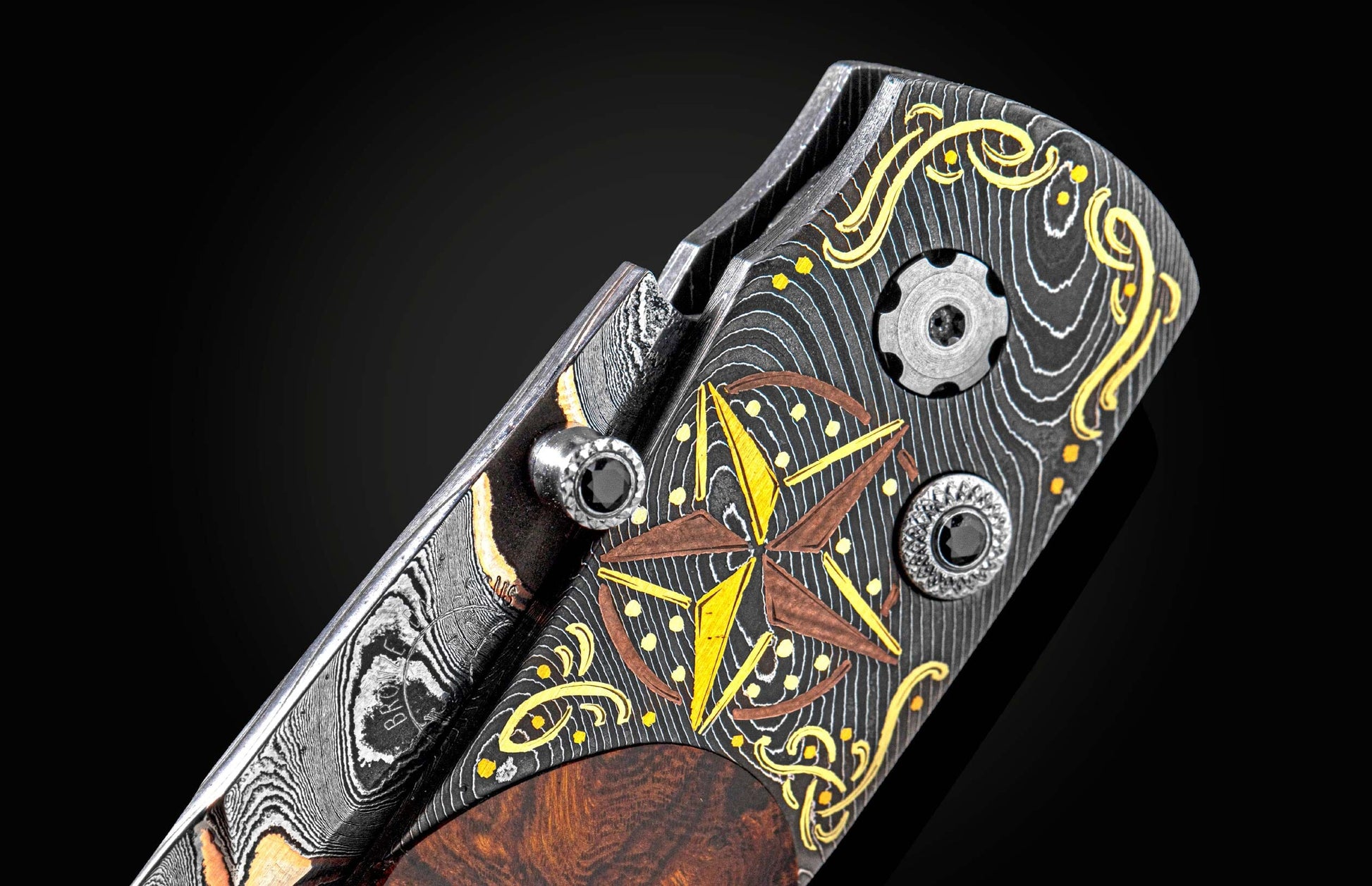 Custom folding knife with patterned Damascus steel and wood handle, featuring a compass rose, gold swirls, black gem accents, and "BRONZE" inscription.