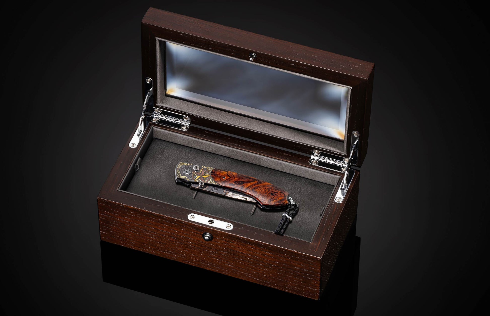 A folding knife with a richly grained brown wooden handle, gold star, and ornate accents, with a Damascus steel blade and black lanyard, displayed in an open dark wood box.