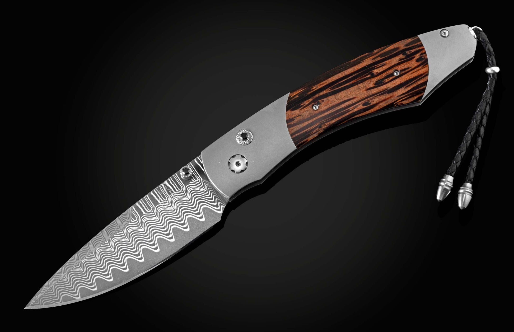 Handcrafted pocket knife from William Henry features a titanium frame inlaid with beautiful Black Palm wood and set with spinel gemstones and a hand forged Damascus steel blade.
