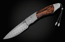 Handcrafted pocket knife from William Henry features a titanium frame inlaid with beautiful Black Palm wood and set with spinel gemstones and a hand forged Damascus steel blade.