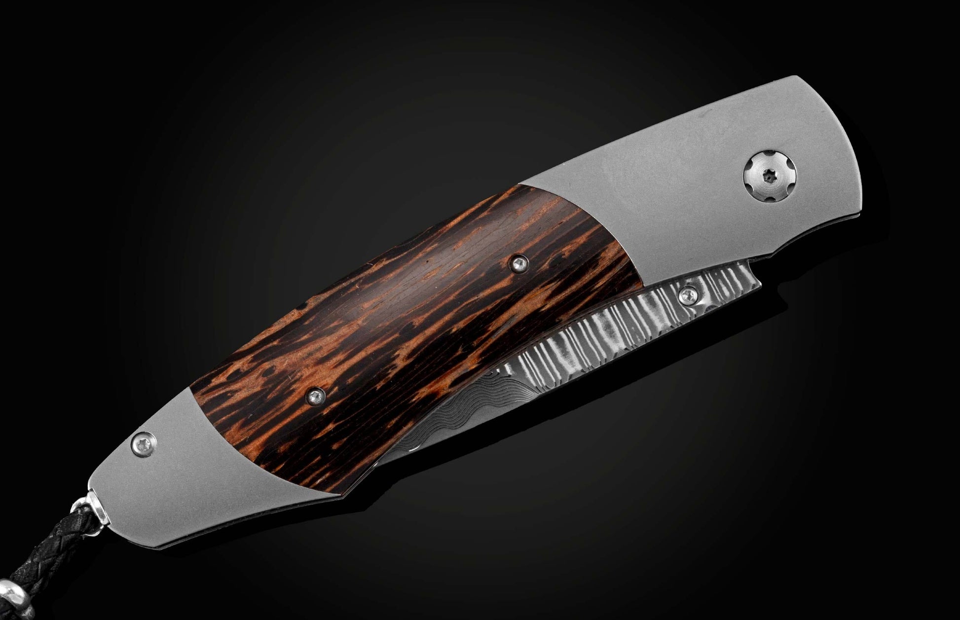Handcrafted pocket knife from William Henry features a titanium frame inlaid with beautiful Black Palm wood and set with spinel gemstones and a hand forged Damascus steel blade.