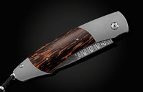 Handcrafted pocket knife from William Henry features a titanium frame inlaid with beautiful Black Palm wood and set with spinel gemstones and a hand forged Damascus steel blade.