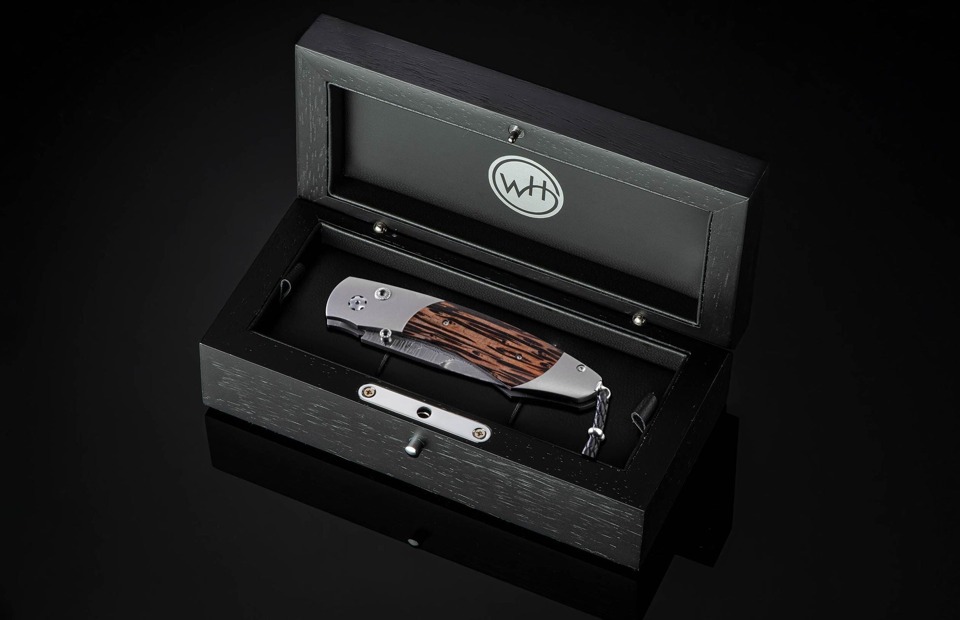 Handcrafted pocket knife from William Henry features a titanium frame inlaid with beautiful Black Palm wood and set with spinel gemstones and a hand forged Damascus steel blade.