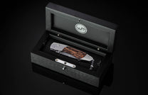 Handcrafted pocket knife from William Henry features a titanium frame inlaid with beautiful Black Palm wood and set with spinel gemstones and a hand forged Damascus steel blade.