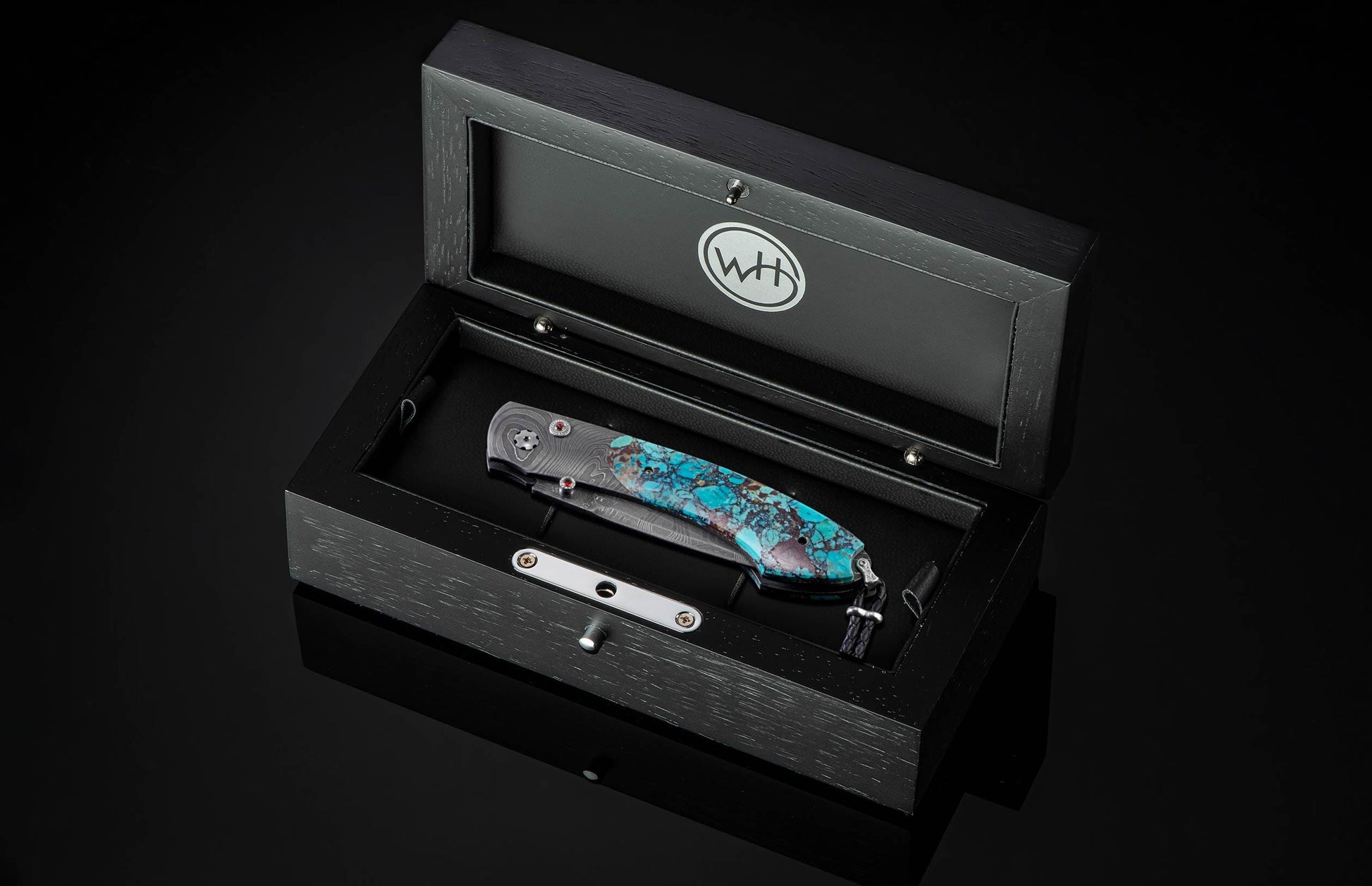 Handcrafted pocket knife from William Henry with a frame in hand-forged Damascus steel inlaid with black Matrix Kingman turquoise and set with garnets. The blade is hand forged damascus steel