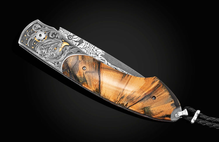 Handcrafted pocket knife from William Henry features hand-engraved bolsters with 24K yellow gold, 18K green and rose gold, and silver, inlaid with fossil Woolly Mammoth tusk and set with spinel gemstones. The blade is hand-forged  damascus steel.