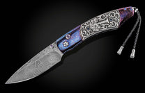 Ornate folding knife with a patterned Damascus steel blade, an engraved silver handle, blue inlays, and a vibrant blue and purple textured grip, with a braided lanyard.