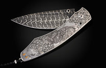 Highly decorative folding knife with a swirling blade pattern and an engraved silver handle featuring a Native American chief and black gemstones.