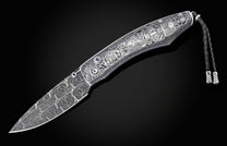 Silver-toned folding knife with intricate steampunk engravings, a patterned blade, blue gemstones, and a braided leather lanyard.