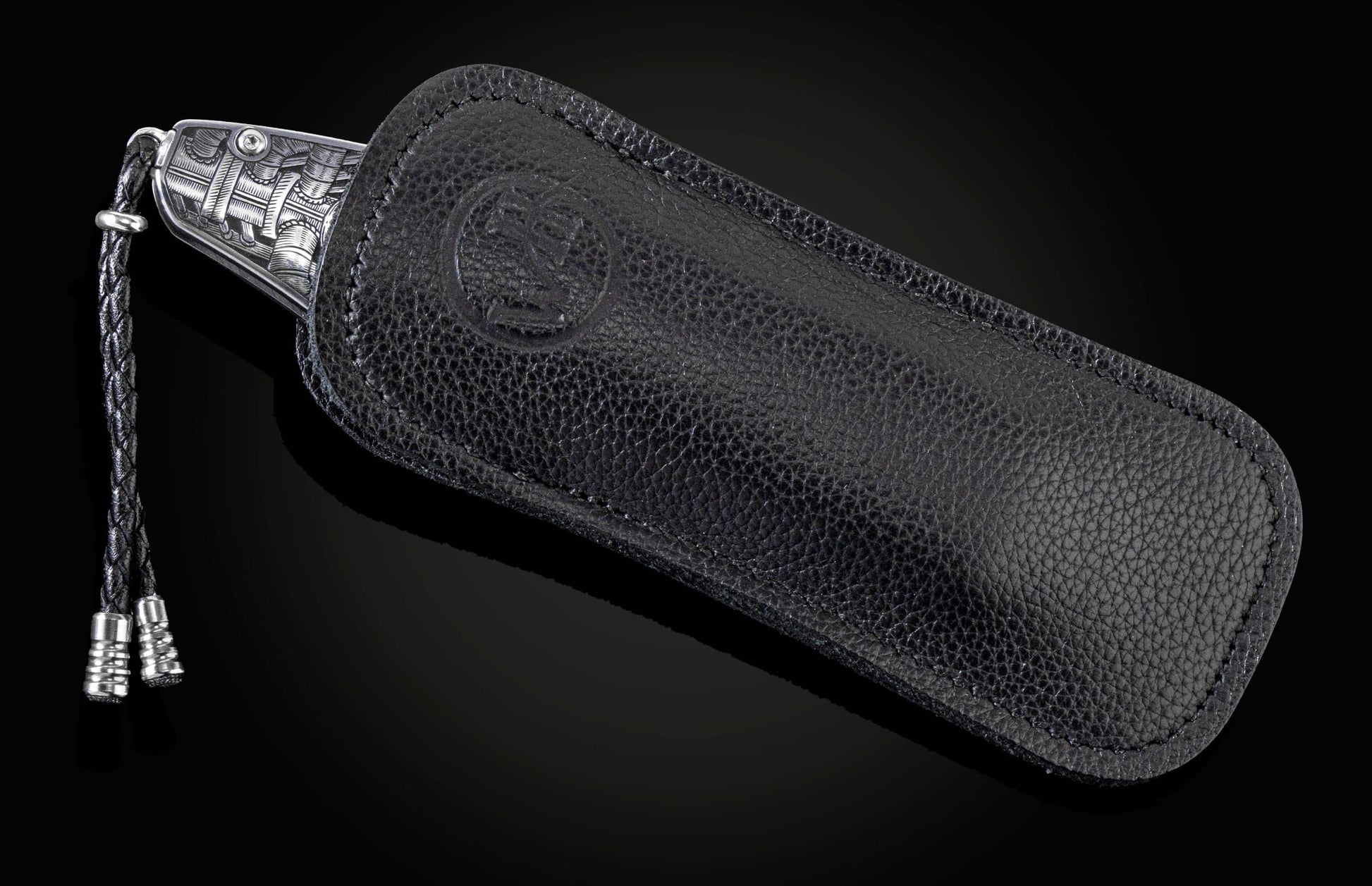 Engraved silver-toned folding knife partially sheathed in black pebbled leather with an embossed logo and braided lanyard.