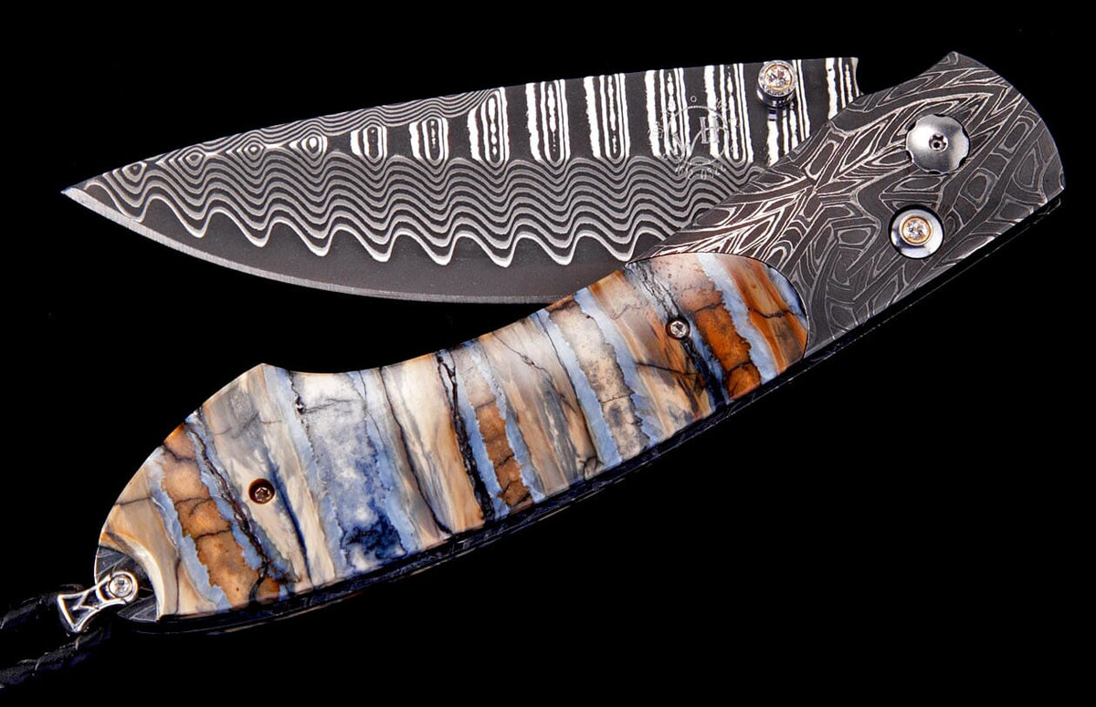 Folding knife by Tamreen with a wavy Damascus blade and a multi-colored, layered handle.