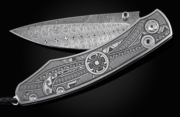 Handcrafted pocket knife from William Henry featuring an engraved tribal motif, a hand-forged Damascus steel blade, and spinel gemstones.