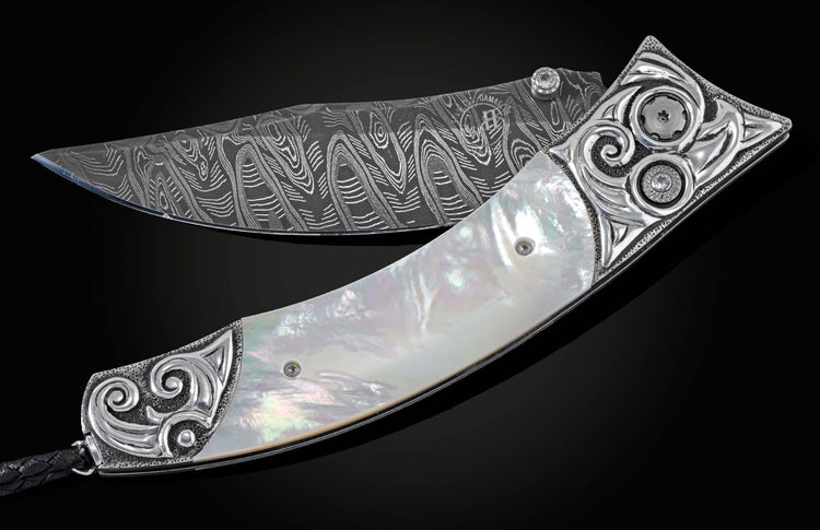 Handcrafted pocket knife from William Henry featuring a frame in hand-carved sterling silver inlaid with mother of pearl. The blade is hand-forged Damascus steel and the button lock and the thumb stud are set with white topaz gemstones. The knife is displ