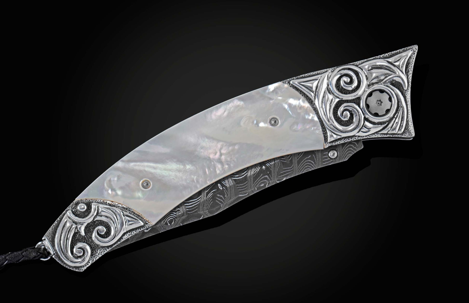 Handcrafted pocket knife from William Henry featuring a frame in hand-carved sterling silver inlaid with mother of pearl. The blade is hand-forged Damascus steel and the button lock and the thumb stud are set with white topaz gemstones. The knife is displ