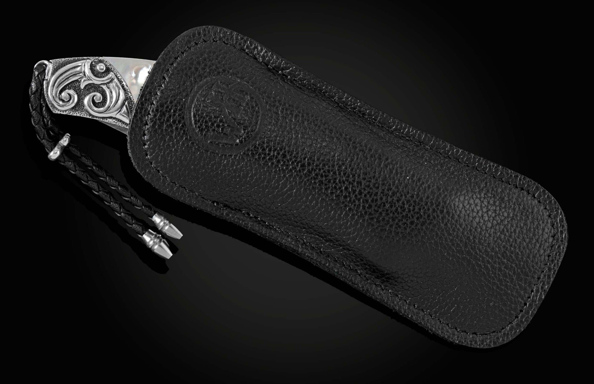 Handcrafted pocket knife from William Henry featuring a frame in hand-carved sterling silver inlaid with mother of pearl. The blade is hand-forged Damascus steel and the button lock and the thumb stud are set with white topaz gemstones. The knife is displ