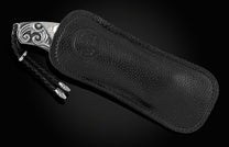 Handcrafted pocket knife from William Henry featuring a frame in hand-carved sterling silver inlaid with mother of pearl. The blade is hand-forged Damascus steel and the button lock and the thumb stud are set with white topaz gemstones. The knife is displ