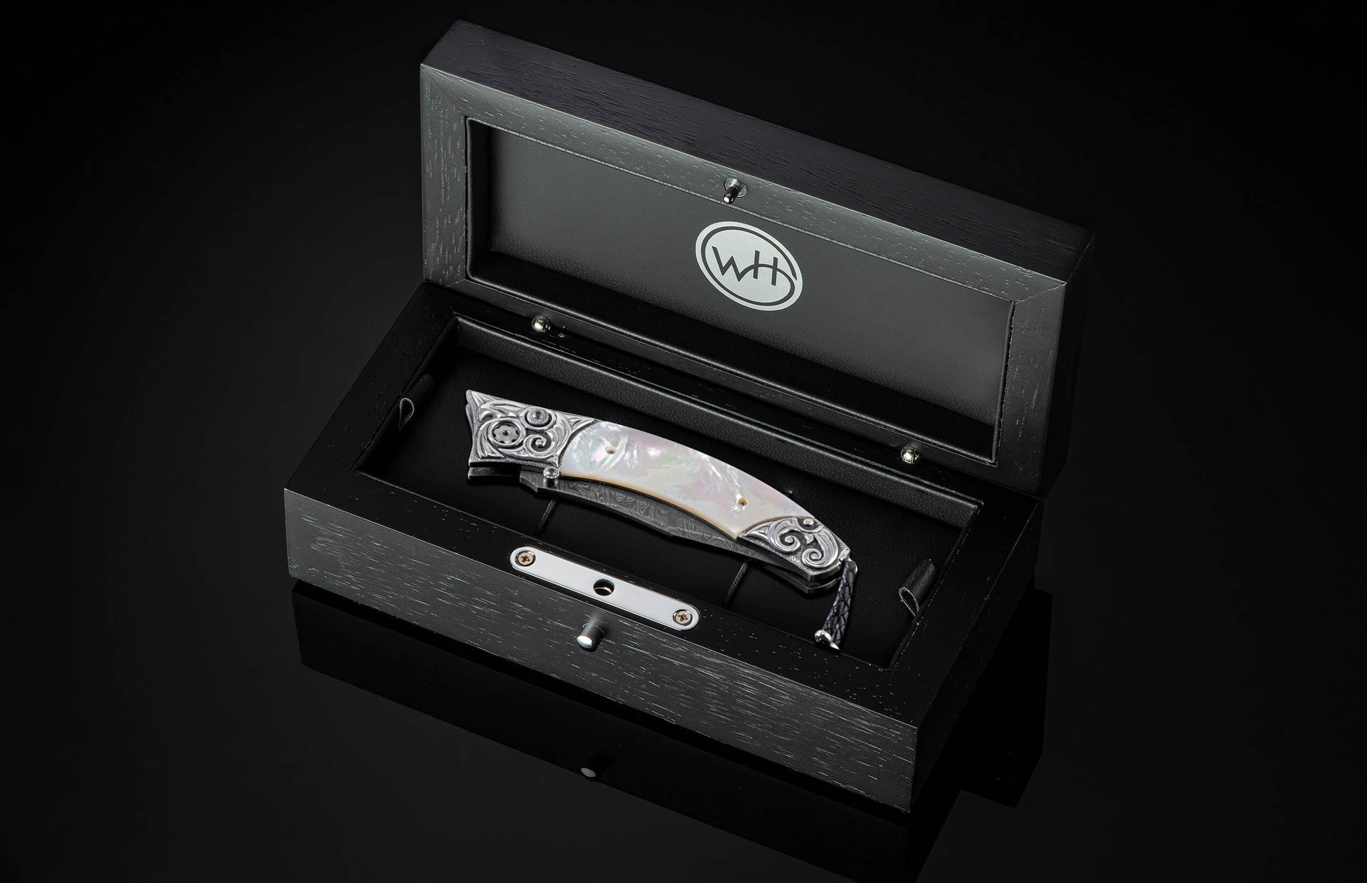 Handcrafted pocket knife from William Henry featuring a frame in hand-carved sterling silver inlaid with mother of pearl. The blade is hand-forged Damascus steel and the button lock and the thumb stud are set with white topaz gemstones. The knife is displ