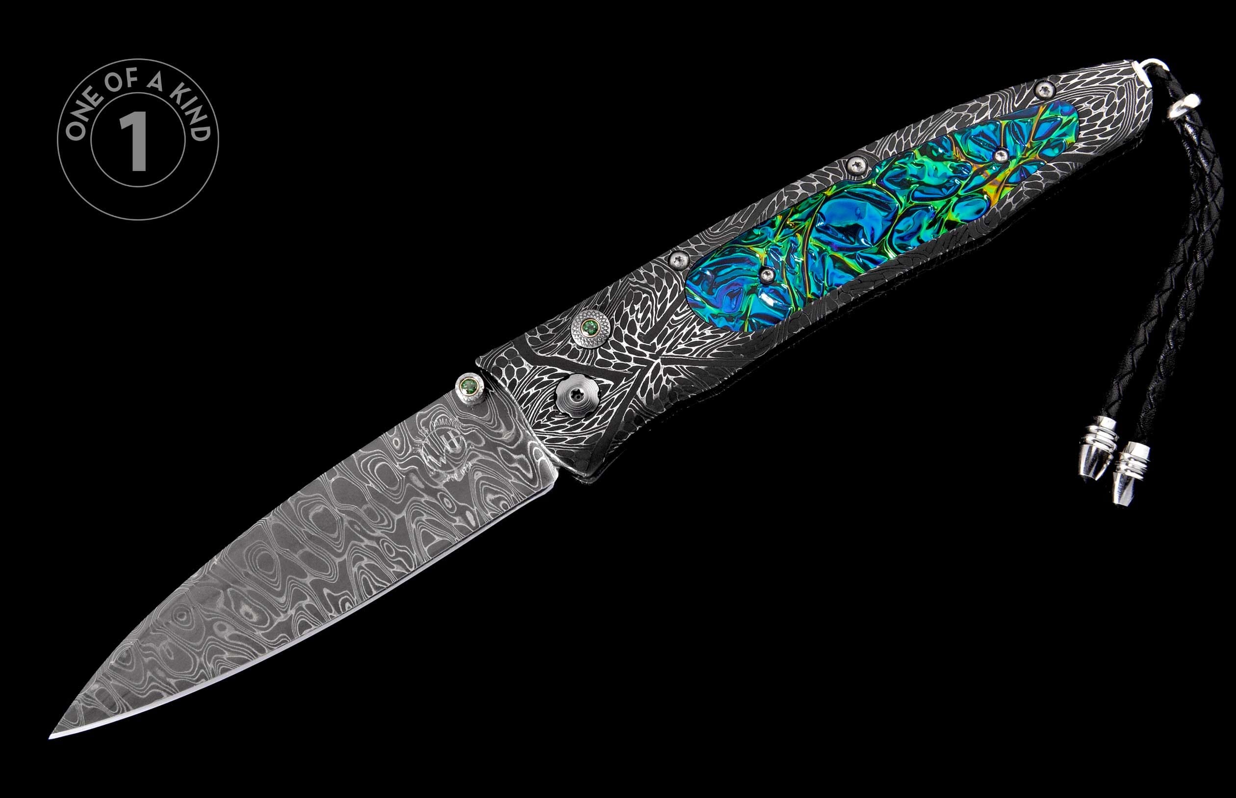 A Damascus steel knife with an etched dark metal handle featuring iridescent blue-green inlay, green gemstone details, and a braided leather lanyard.