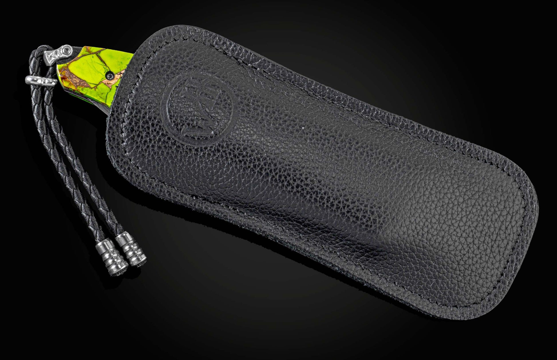 Knife with vibrant green and brown handle partially inserted into a black textured leather case with an embossed logo and braided lanyard.