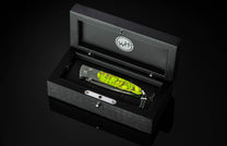 Folding knife with a Damascus steel blade and lime green textured handle, presented in an open black wooden box with a 'WH' logo.