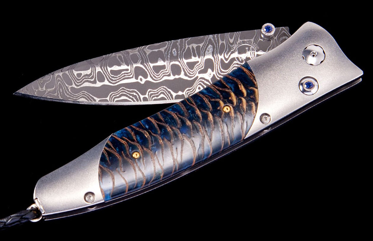 Elegant folding knife by Tamreen with a patterned Damascus steel blade, a blue-gold fish scale handle, and sapphire pivot accents.