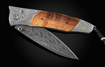 Open folding knife with a wavy Damascus steel blade, dark wood handle, and engraved silver bolsters featuring a golden feather and Liberty Bell.