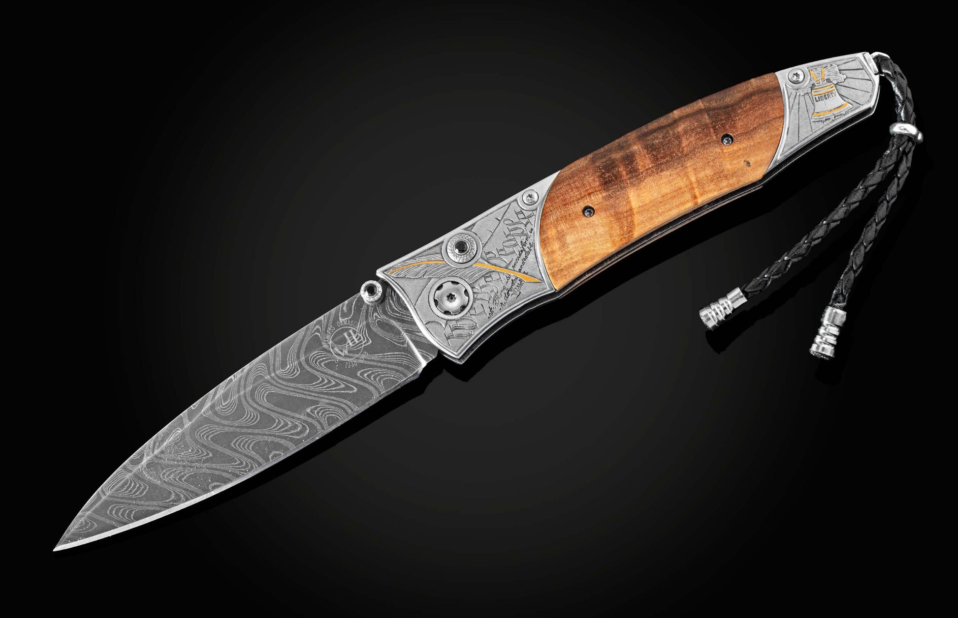 Knife with a wavy Damascus steel blade, polished light brown wood handle, and engraved silver bolsters featuring a Liberty Bell.