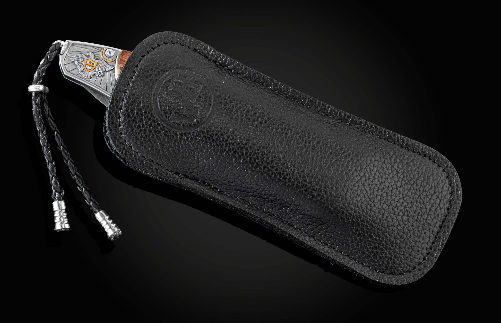 B30 Washington knife with a silver eagle handle and braided lanyard, partially in a black pebbled leather sheath with an embossed logo.