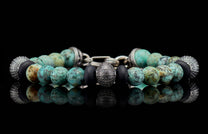 Beaded bracelet with mottled turquoise, matte black, and textured silver beads on a reflective surface.
