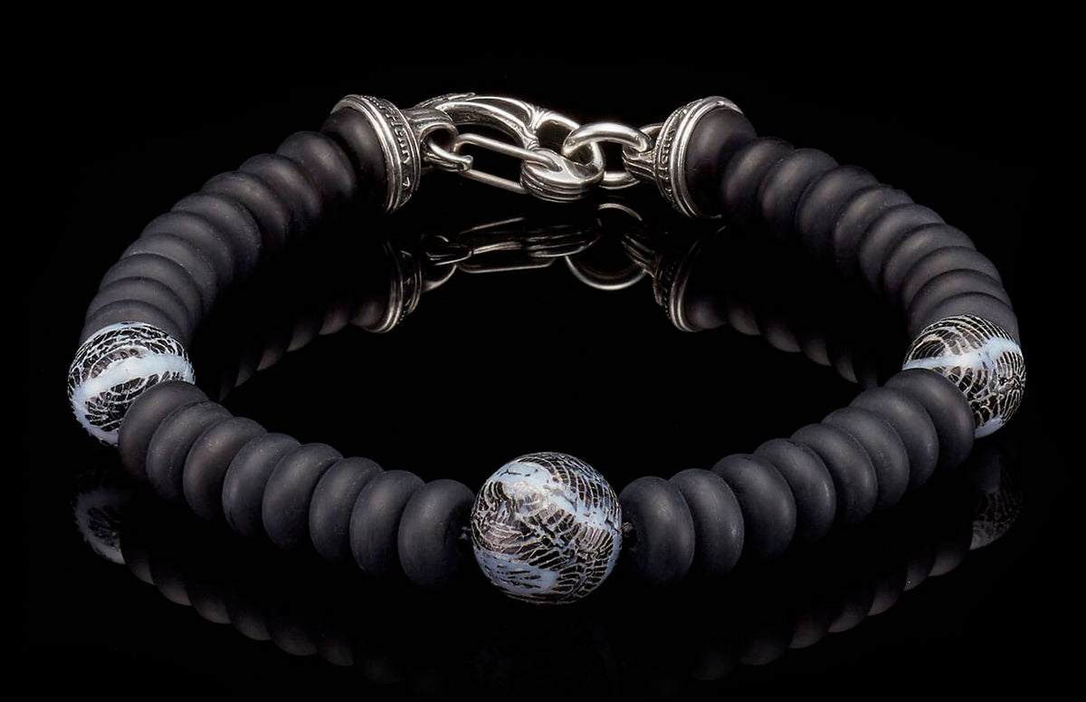 Matte black beaded bracelet with a silver hook clasp and three patterned white and black glass accent beads.