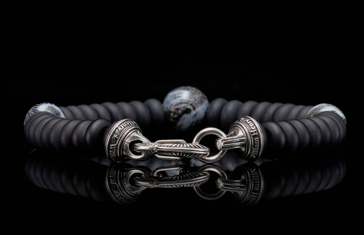 Matte black beaded bracelet with an ornate silver-tone clasp featuring engravings, a central patterned bead, and a strong reflection.
