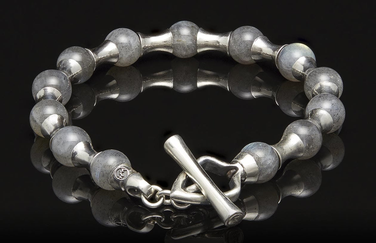 Silver-tone beaded bracelet with grey stone beads, featuring alternating metal links and a toggle clasp, on a reflective surface.